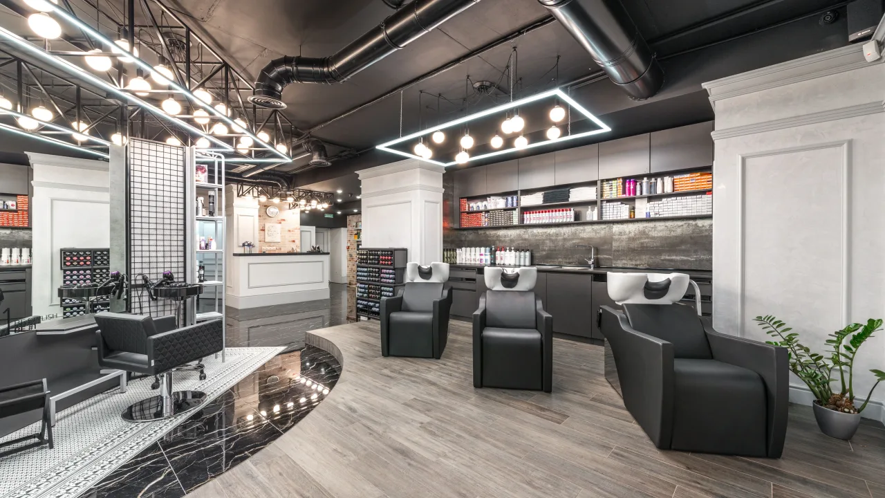 A modern hair salon with black styling chairs, shampoo basins and pendant lights